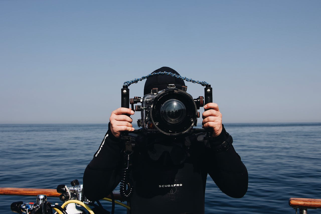 Services A scuba diver holding an underwater camera setup while on a boat by the sea.