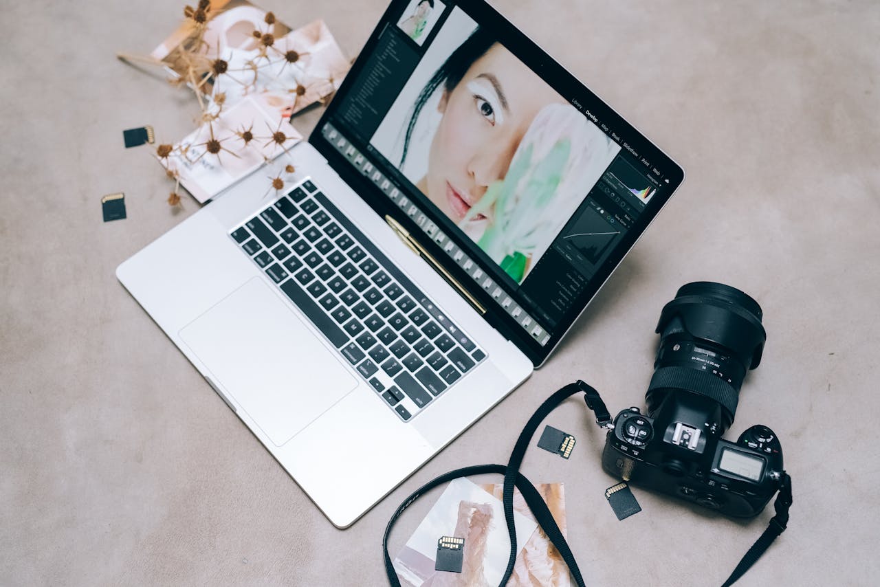 Flat lay of a laptop with photo editing software, camera, and memory cards on a desk.